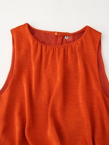 Detail view of the orange sleeveless top featuring neck pleats and back button closure