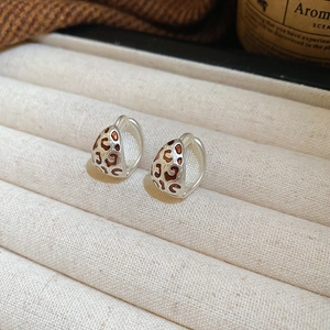 Détail de boucles d'oreilles créoles en émail léopard sur plateau en velours beige