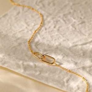 Close-up of interlocking oval rings on a 18K gold plated chain necklace set on textured paper