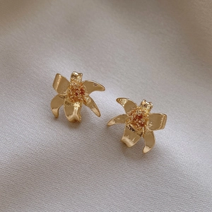 Detailed close-up of matte gold flower earrings on elegant textured satin background
