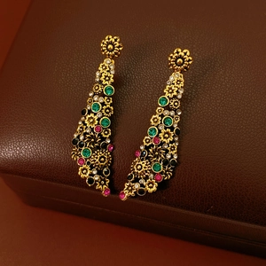 Détail de boucles d'oreilles fleurs dorées vintage avec cristaux multicolores sur cuir