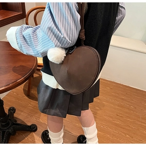 Detail der dunkelbraunen Herz-Handtasche in Mattoptik mit weißem Kunstpelz-Anhänger