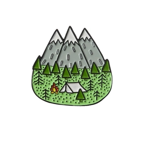 Close-up of enamel mountain brooch with forest camping tent and campfire design