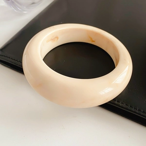 Detailed view of wide resin bangle with cream and tan marble texture on black leather