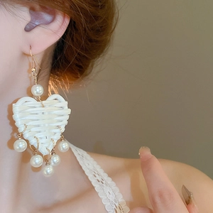 Détail de la boucle d'oreille cœur en raphia crème tissé avec perles sur le mannequin