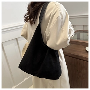 Detailed view of black suede shoulder bag with wide strap on model's shoulder