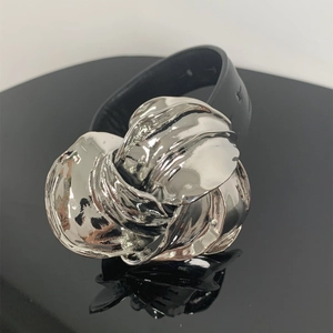 Detail van de zilveren metalen bloemgesp op een zwarte leren riem met spiegelreflectie