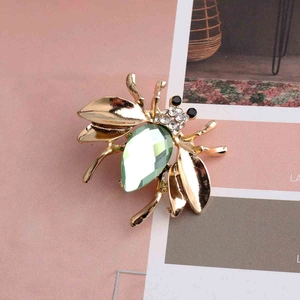 Macro view of bee brooch featuring a light green pear-cut gem and white diamonds