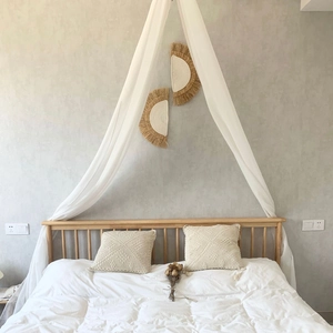 Boho style half-round handmade woven raffia wall decor above a white canopy bed