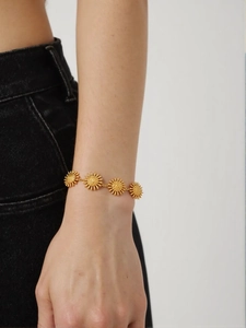 Detail view of 18k gold sun charm bracelet with radial texture on a model's wrist