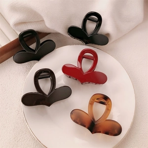Minimalist heart-shaped hair claw clips in black, wine red, and amber colors on ceramic plate