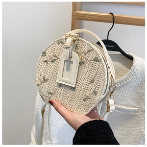 Detail of floral embroidery on a circular straw bag with leather straps and gold zipper