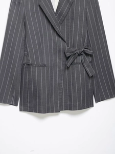 Detail of dark grey striped blazer featuring a waist tie bow and flap pocket design