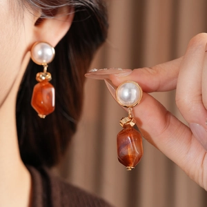 Close-up of amber resin pearl earrings with gold metal accents worn by a model
