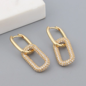 Detail of gold geometric hoop earrings with sparkling cubic zirconia on marble background