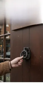 Detail of vintage iron door knocker on wood showing antique texture and hand interaction