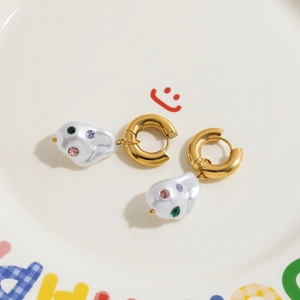 Detail of gold hoop earrings with irregular pearl charms and colorful inlaid gemstones
