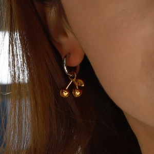 Close-up of elegant gold cherry pendant earrings worn by a model in soft lighting