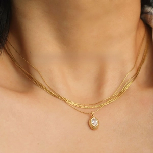 Close-up of a layered gold chain necklace featuring an oval pendant with a clear zircon stone