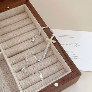 Detail of S925 sterling silver cross bracelet on beige velvet inside a wooden jewelry box