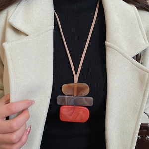 Detail of geometric acrylic pendant necklace in brown, grey and red on black turtleneck