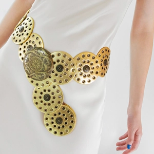 Close-up of a vintage golden metal waist belt with engraved circular discs on a white dress
