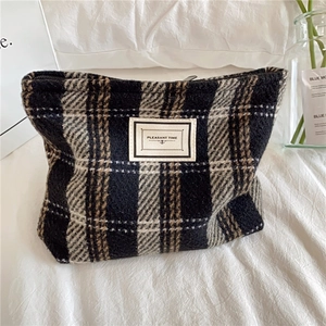 Detailed view of plaid tweed makeup bag with Pleasant Time label on soft bedding