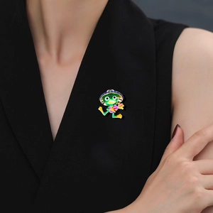 Close-up of a cute green enamel frog brooch with a straw hat pinned on a dark coat