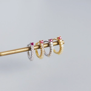 Macro shot of silver and gold huggie hoop earrings with red stones and zircon pavé
