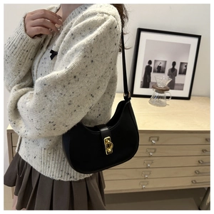 Détail du sac demi-lune en cuir noir avec boucle dorée vintage sur l'épaule de la femme