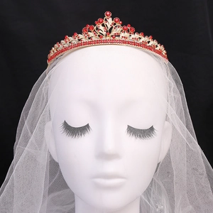 Detail of a gold bridal crown with red rhinestones and white mesh veil on a mannequin