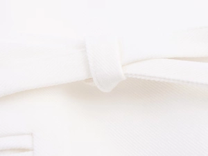 Detailed close-up of white linen blend fabric texture and refined waist belt loop stitching