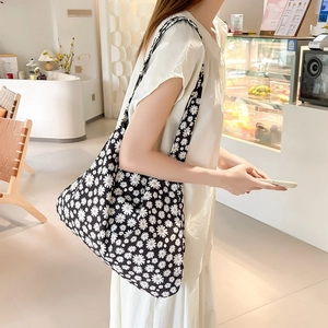 Detailed view of black canvas tote bag with white daisy patterns in a bright cafe setting