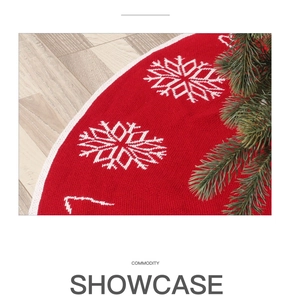 Close-up of red knitted Christmas tree skirt with white snowflake patterns on wood floor