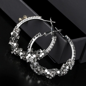 Close-up of silver irregular pleated C-shaped hoop earrings with sparkling rhinestones