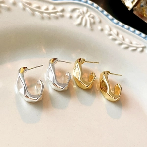 Detail of irregular C-shape earrings in gold and silver on a vintage ceramic plate
