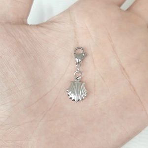 Macro view of a silver shell pendant with lobster clasp held in hand for scale