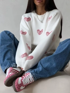 Detail of white crewneck knit sweater featuring red heart embroidery and casual blue denim