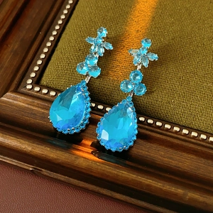 Vue détaillée des boucles d'oreilles gouttes bleu aqua avec fleurs sur tissu vert rétro