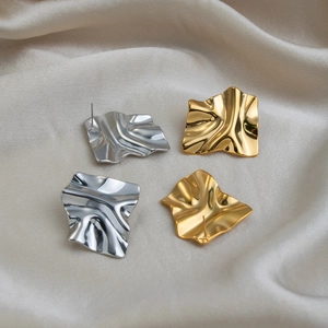 Macro view of geometric pleated earrings in gold and silver finish on silk fabric