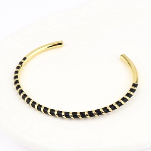 Detail of bohemian gold and black enamel stripe cuff bracelet on a white display base