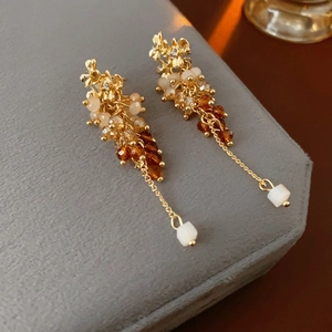 Detail of vintage gold tassel earrings with gradient beads on a grey hexagonal display stand