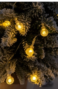 Close-up of LED bubble ball string lights with warm glow on snow-covered Christmas tree