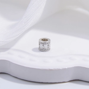 Cylindrical S925 silver bead with white cubic zirconia inlay and relief carvings on ceramic plate