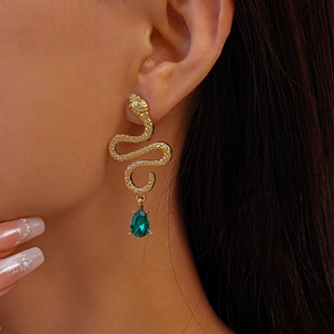 Detailed view of gold snake earrings with green teardrop pendants on a model