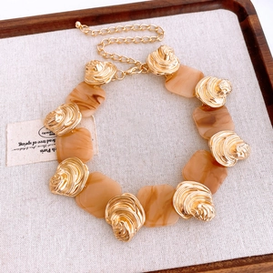 Close-up of a gold shell and brown resin square pendant necklace on a wooden tray