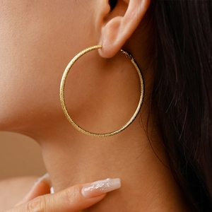 Close-up of model wearing large gold hoop earrings with a matte metallic finish