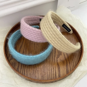 Detailed knit texture of plush headbands in pink, beige and light blue on wood
