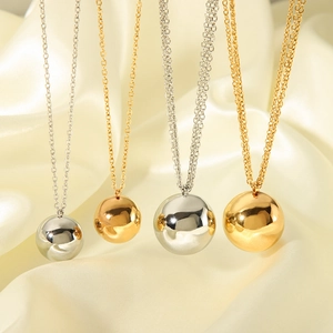 Polished 18K gold and silver ball pendant necklaces on elegant cream silk fabric