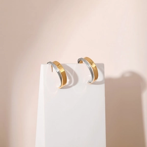 Minimalist C-shape two-tone earrings in gold and silver finish on a white display pedestal